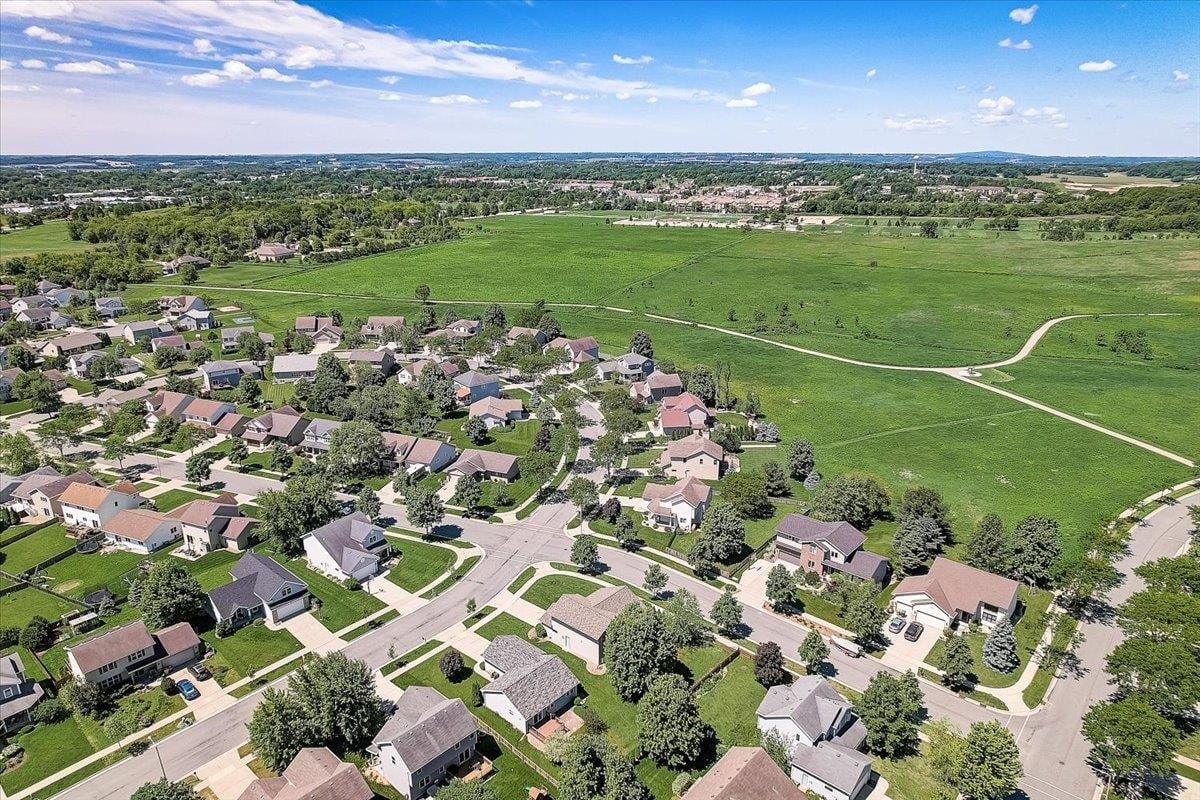 Aerial view of a Dane County, Wisconsin neighborhood in summer, with curving streets of single-family homes bordering open green space.