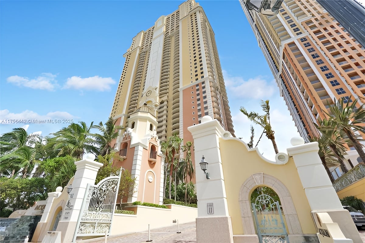 Acqualina high-rise residences behind an ornate entrance gate, framed by palm trees.