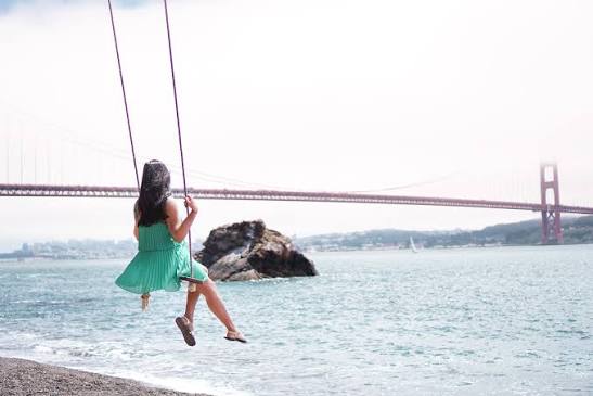Woman on swing overlooking San Francisco Bay with Golden Gate Bridge in distance