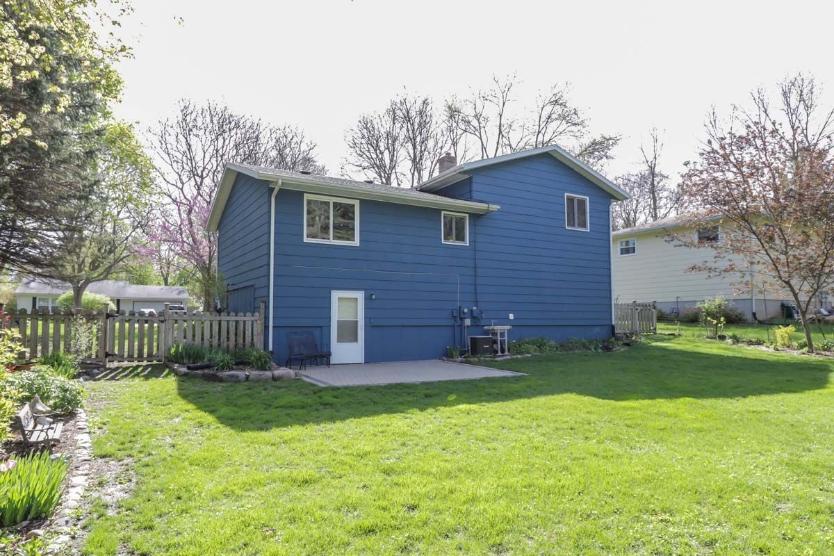 Blue two-story house viewed from a fenced backyard with a broad lawn and garden beds.