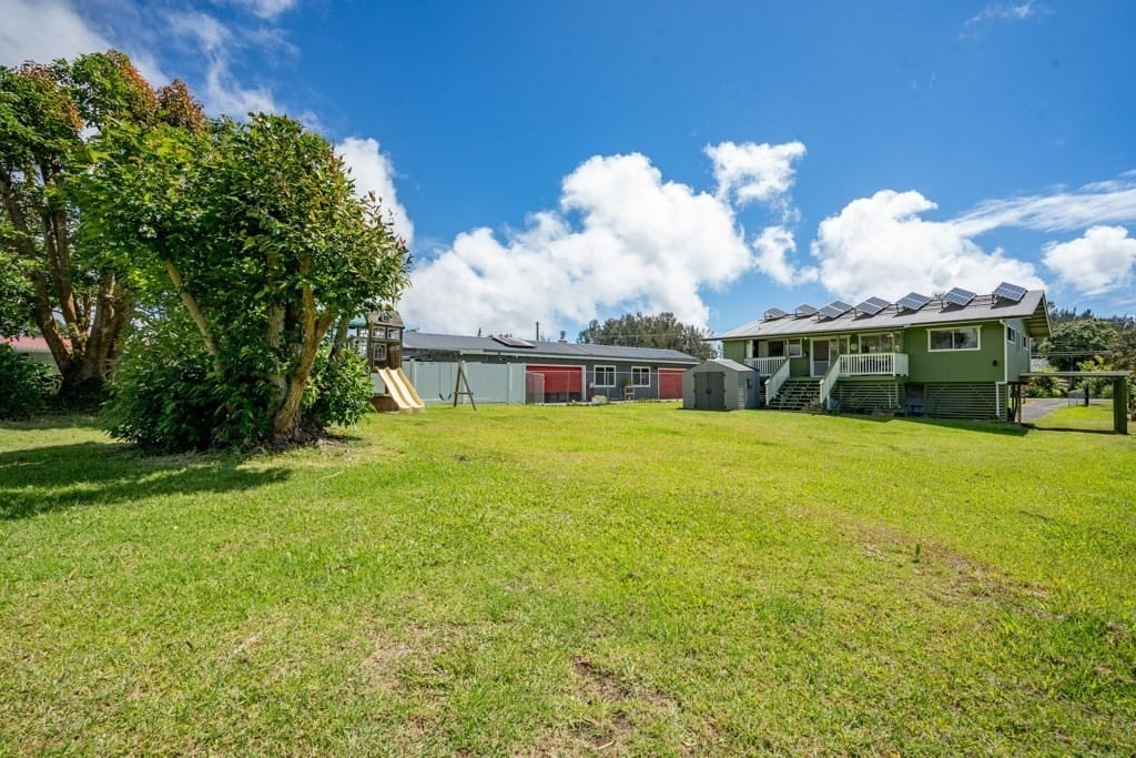 Large grassy backyard with mature trees, a playset, and a green home topped with solar panels.