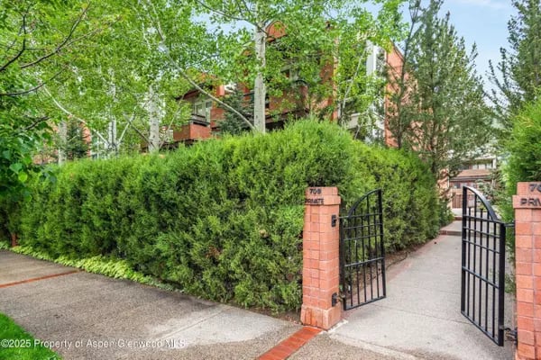 Residential entrance with black metal gates, brick pillars, and tall hedges in front of a brick building.