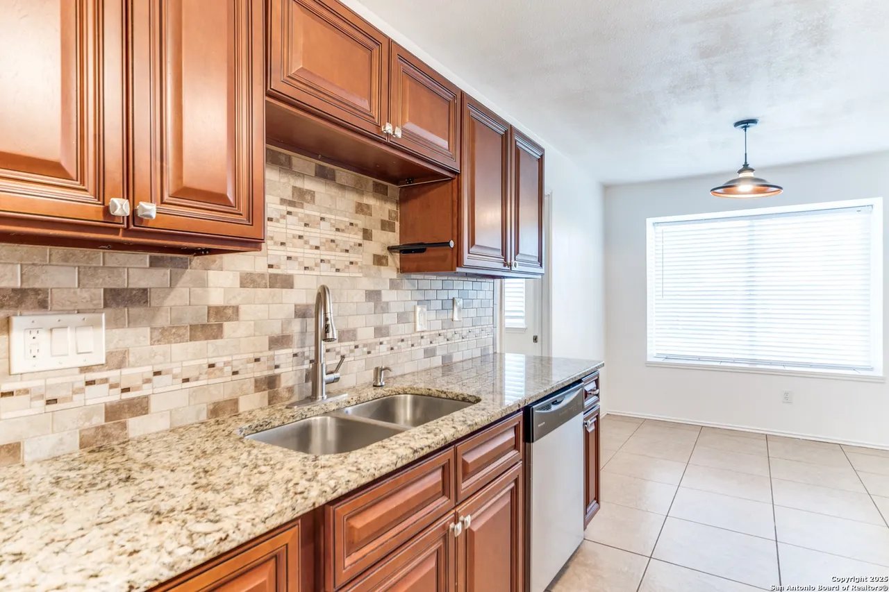 Kitchen with reddish-brown cabinets, granite counters, double sink, and multitone tile backsplash.