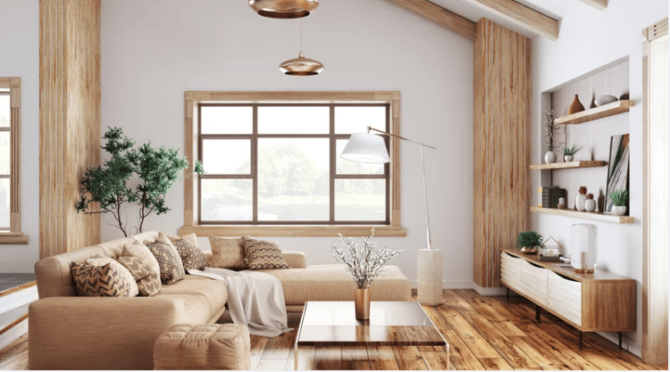 Staged living room with a beige sectional, bright window, exposed wood beams, and hardwood floors.