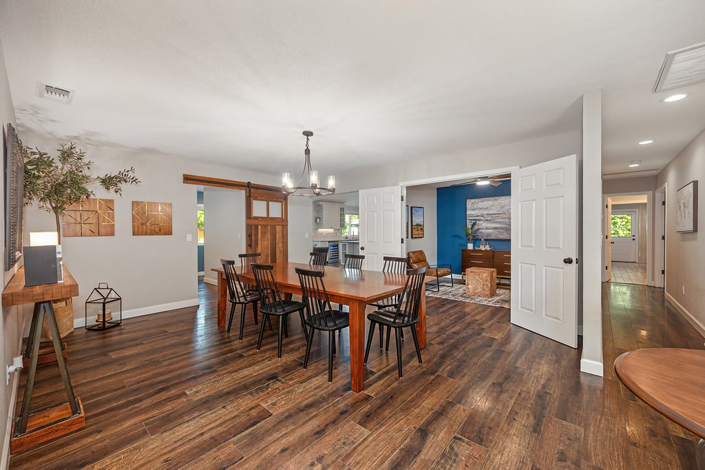 Dining room with a long wooden table, black chairs, and a barn door opening to a blue living room.