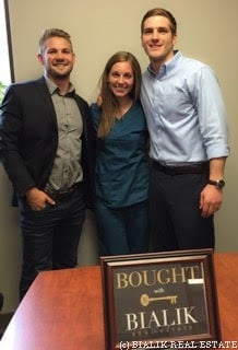 Three people celebrating a home purchase beside a “Bought by Bialik” sign.