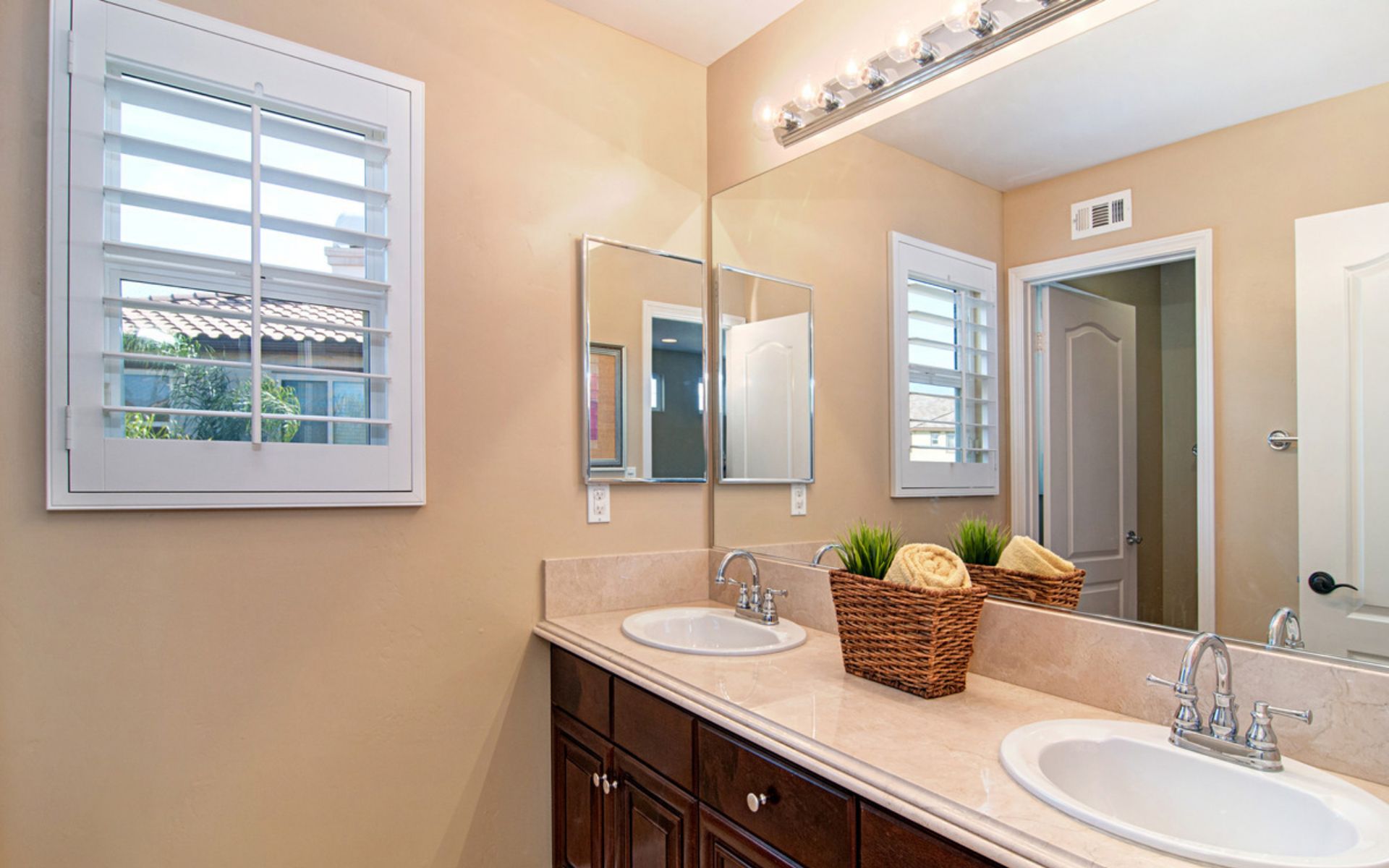 Bathroom double vanity with dark wood cabinets, pale stone counter, and baskets of towels.