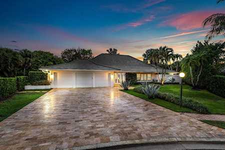 Single-story home with a wide paved driveway and palm-lined landscaping at dusk.