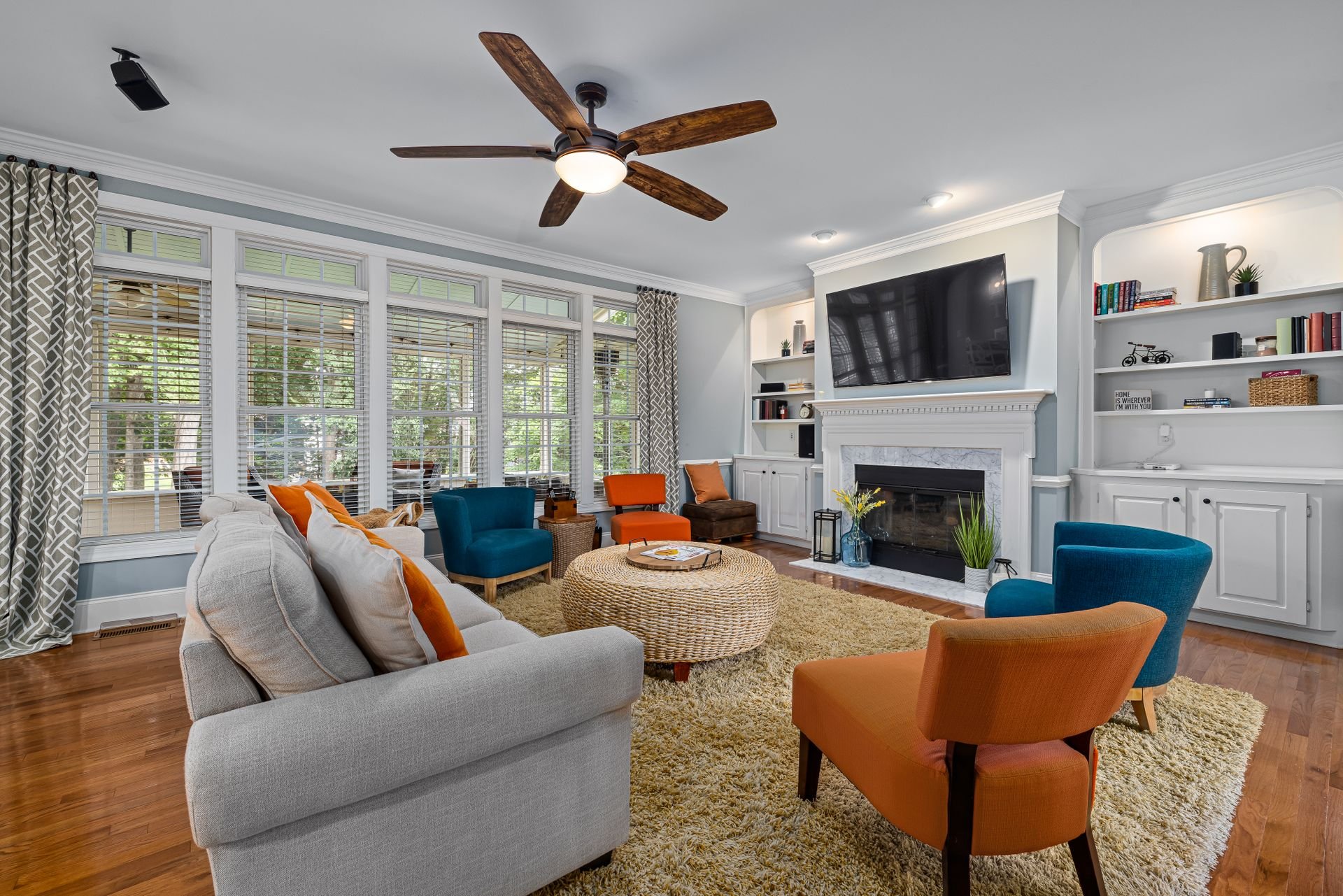 Furnished living room with tall windows, colorful chairs, built-in shelves, and a white fireplace.