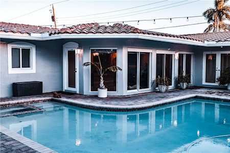 Blue stucco home with broad glass doors facing a curved swimming pool at dusk.