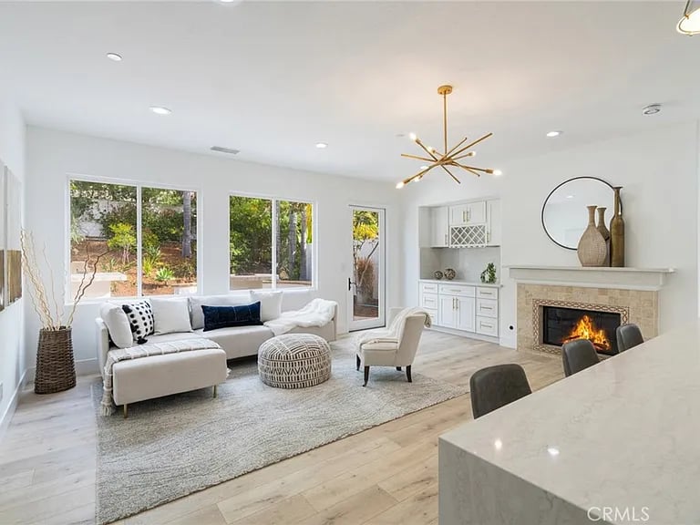 Bright living room with a white sectional, large windows, and a lit fireplace.