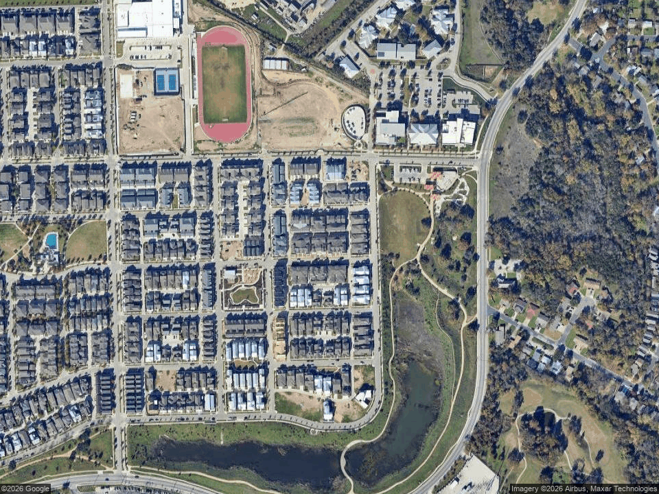 Aerial view of homes beside a winding creek, wooded greenbelt, and school running track.