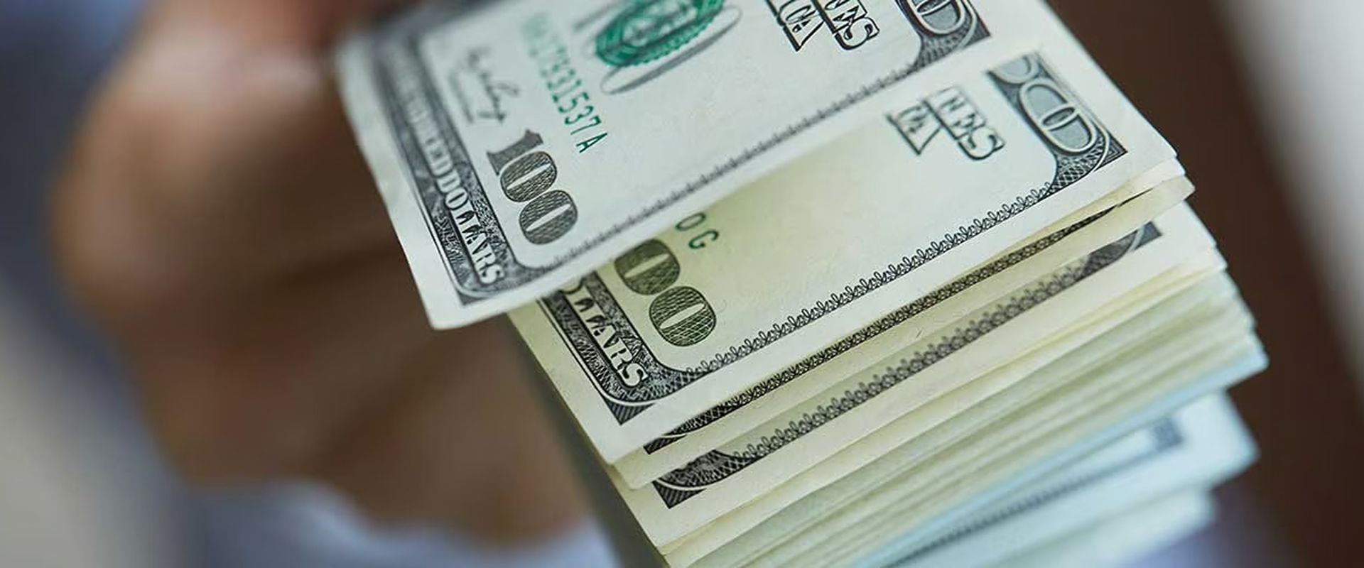A stack of U.S. $100 bills, with several banknotes fanned across the top.