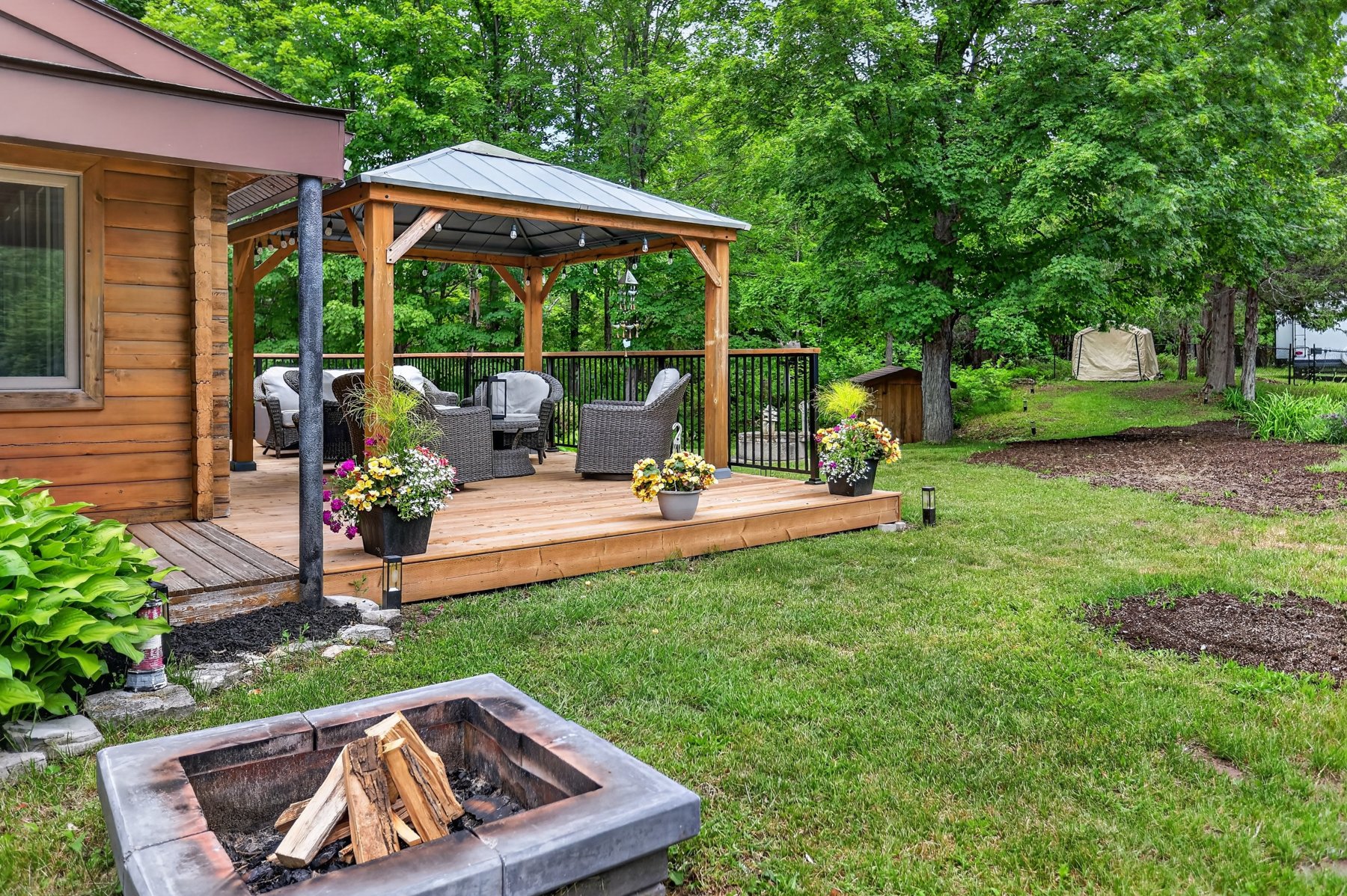 Cottage backyard with a furnished gazebo deck and a stone fire pit in the foreground.