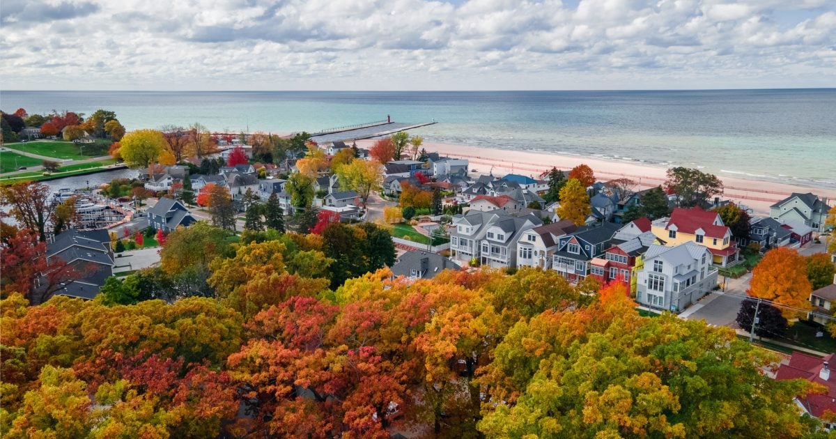 Aerial view of South Haven, Michigan in fall with colorful trees, lakeside homes, and the pier leading to the red lighthouse.