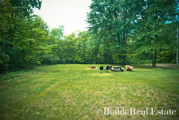 Grassy clearing bordered by mature trees, with a picnic table and chairs.