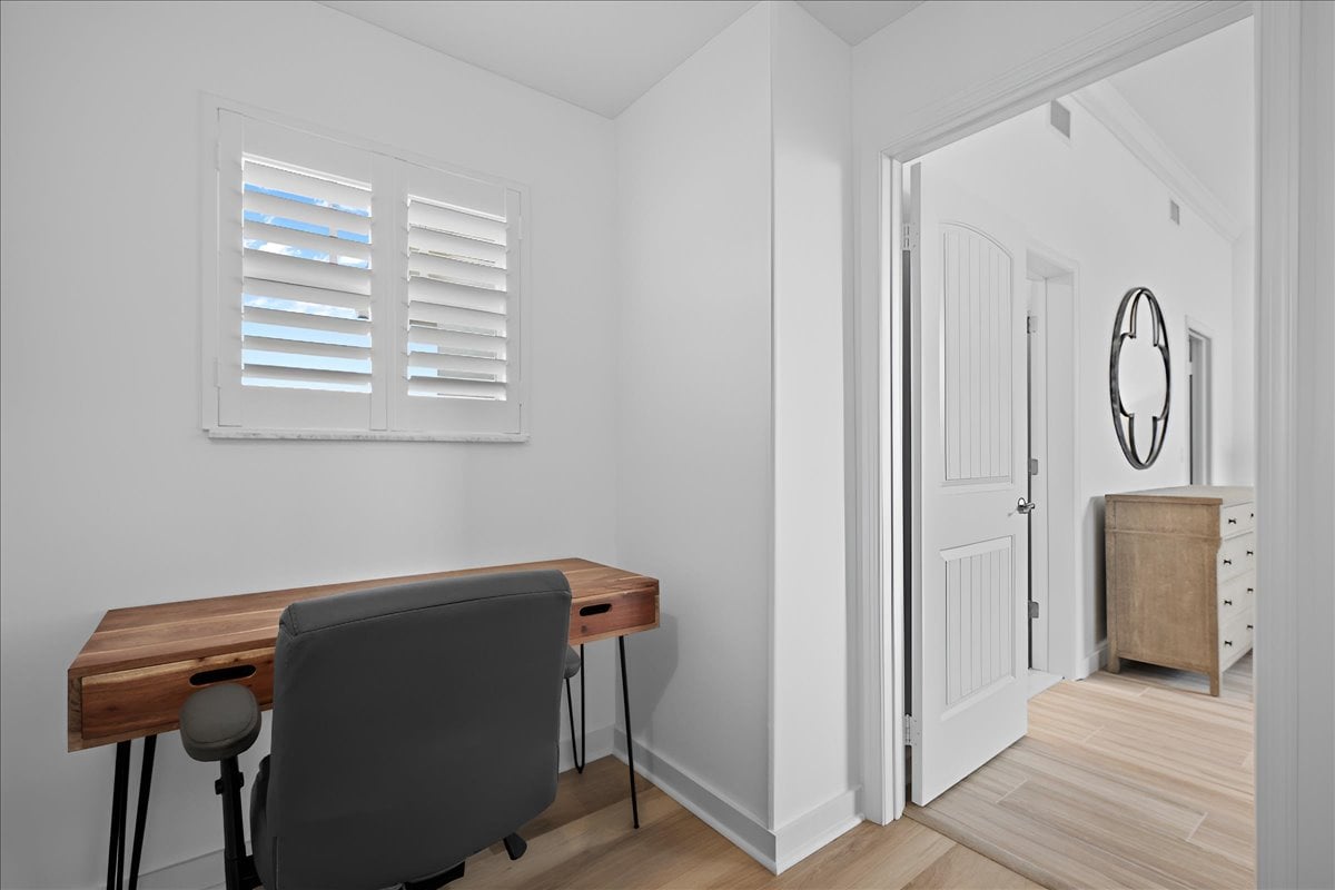 Office nook with a wood desk beneath plantation shutters, opening onto a bright hallway.