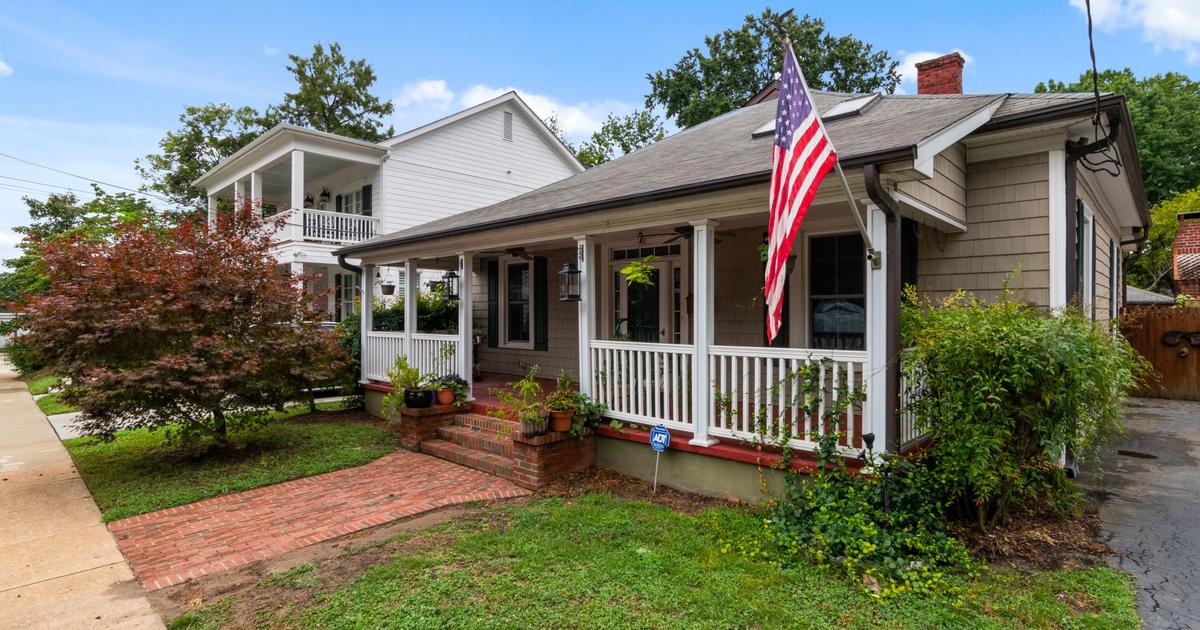 House with a covered front porch, American flag, and brick walkway.