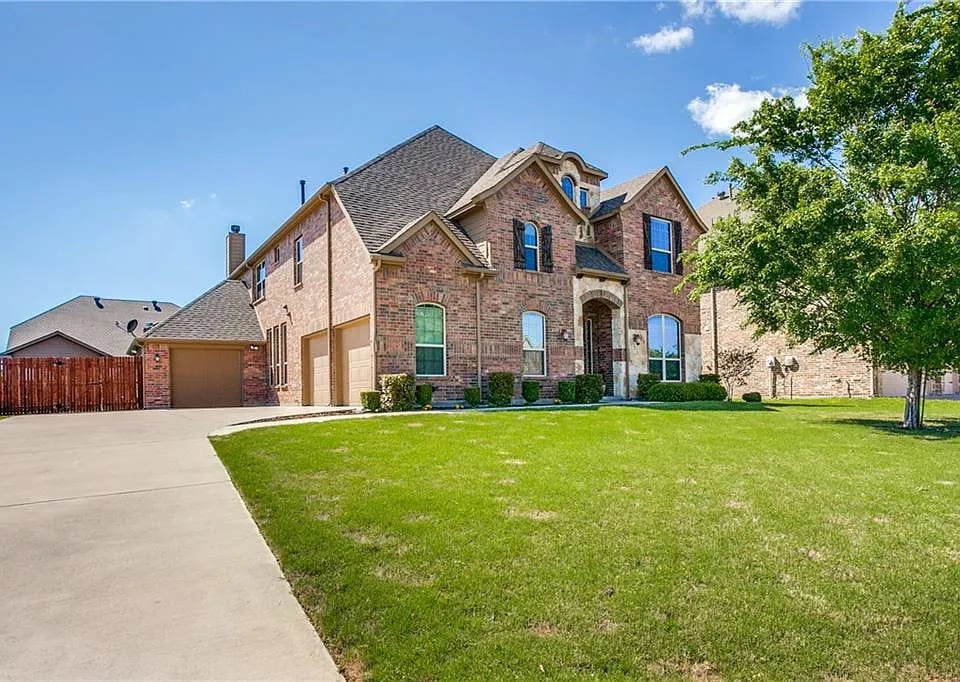 Two-story brick house with an attached garage, wide driveway, and broad green lawn.