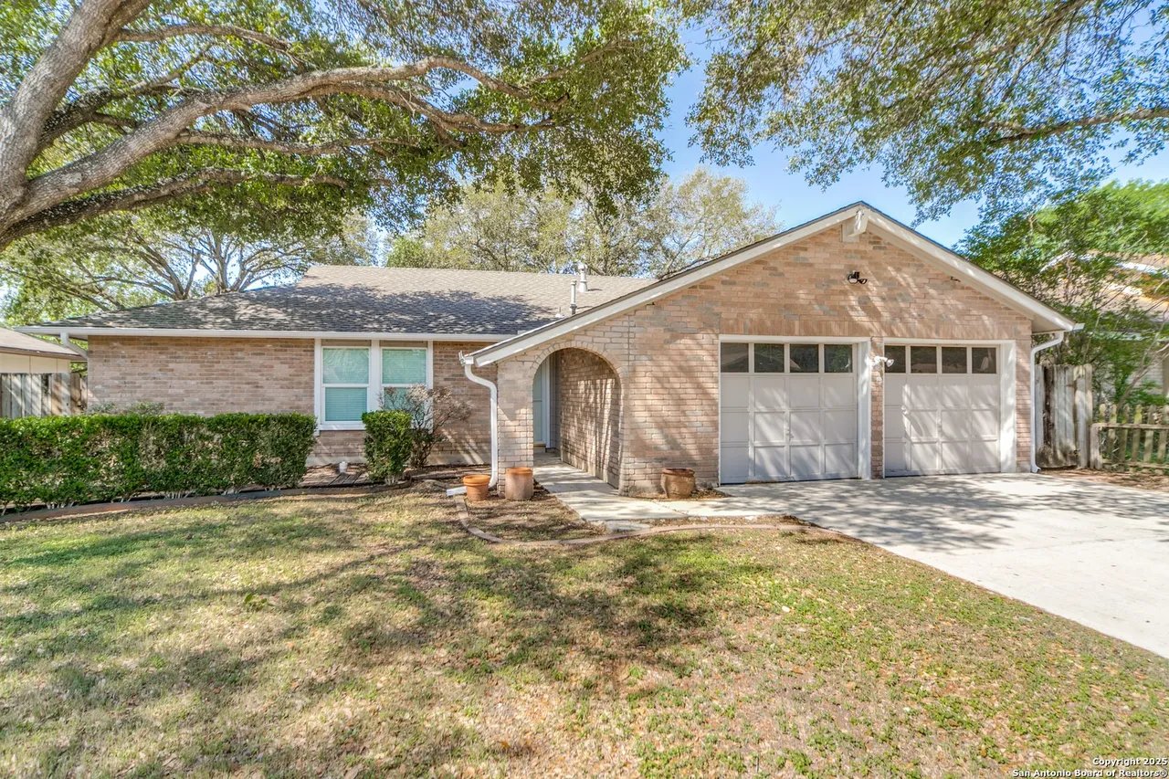 Brick home with a two-car garage and arched entry beneath a large shade tree.