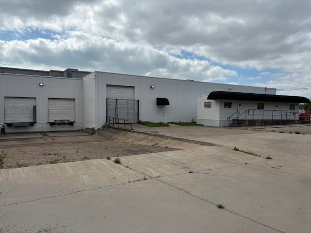 Industrial warehouse exterior with loading docks, a covered entrance, and a broad paved lot.