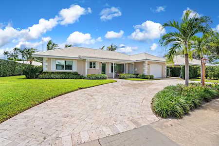 Single-story home with a curved paver driveway, green lawn, and palm trees.