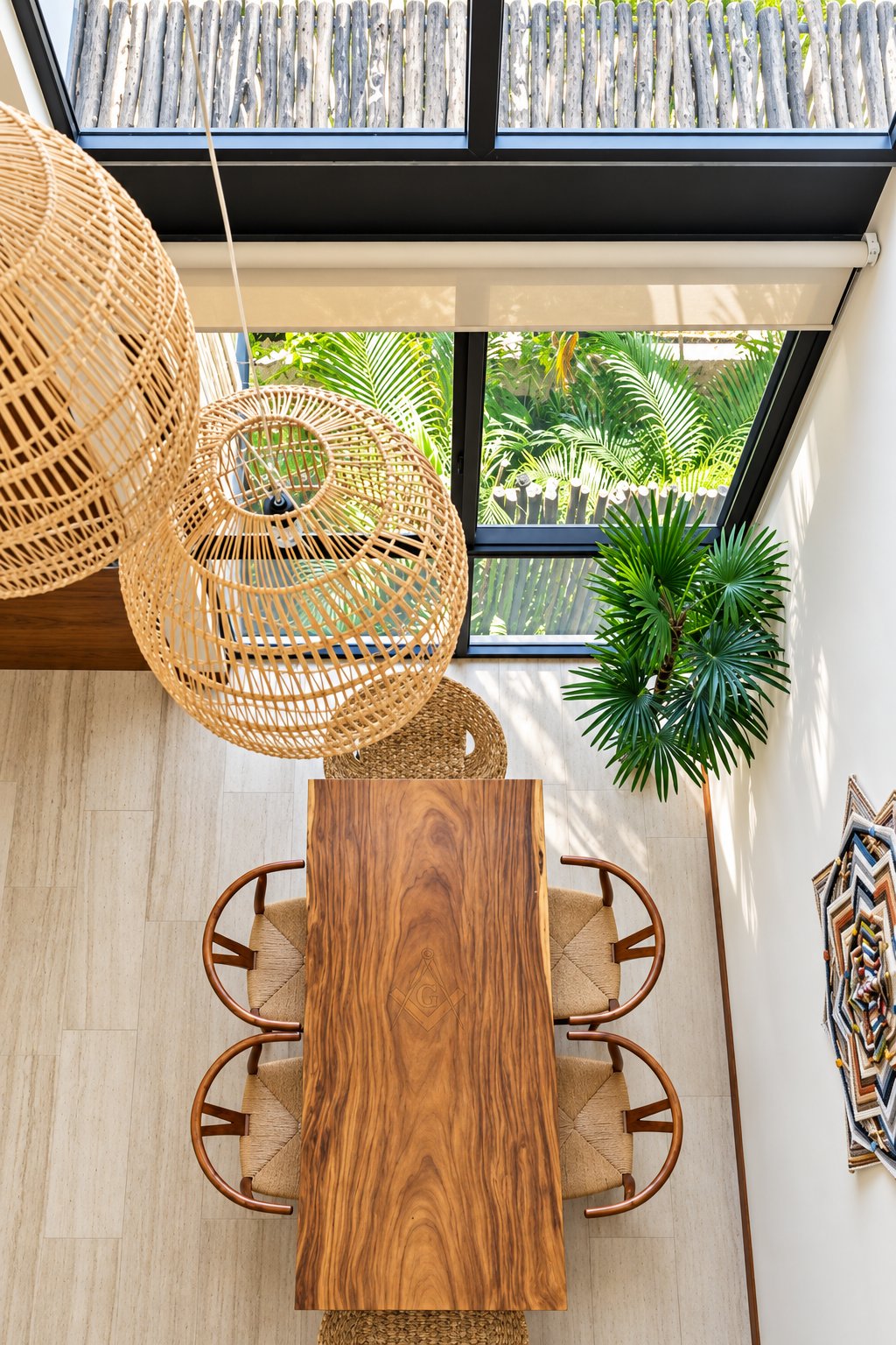 Dining area with a long wooden table, woven chairs, hanging rattan seats, and skylights overlooking tropical greenery.