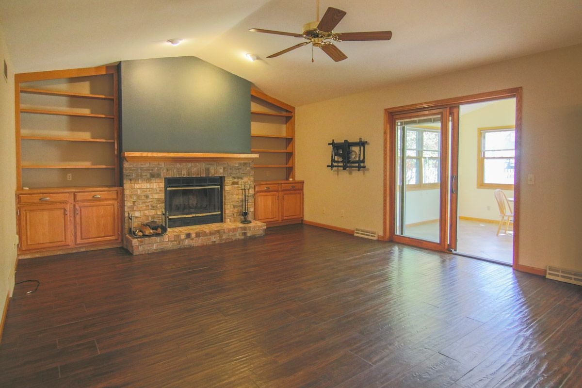 Living room with a brick fireplace, built-in wooden shelving, dark hardwood floors, and a sliding glass door.