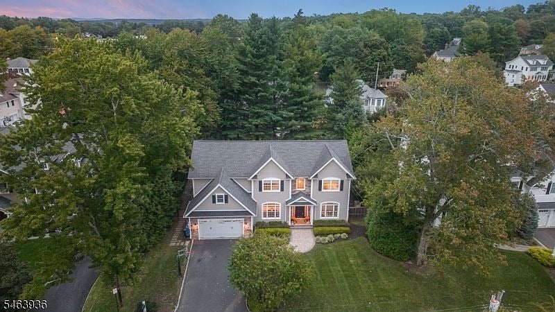 Gray two-story house with an attached garage, seen from above among mature trees at dusk.