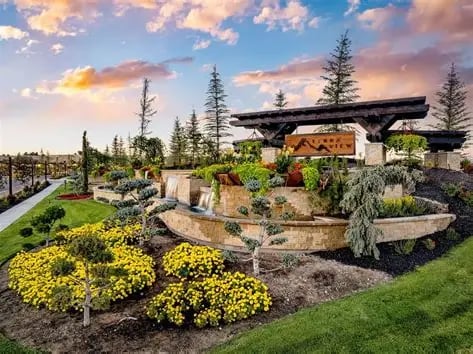 Landscaped pavilion area with curved stone walls, yellow flowers, and a paved path.