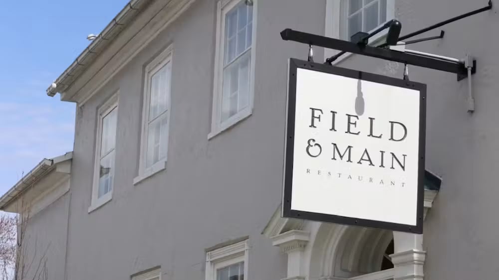 Hanging sign reading "Field & Main Restaurant" outside the gray stucco building on Main Street in Marshall, Virginia