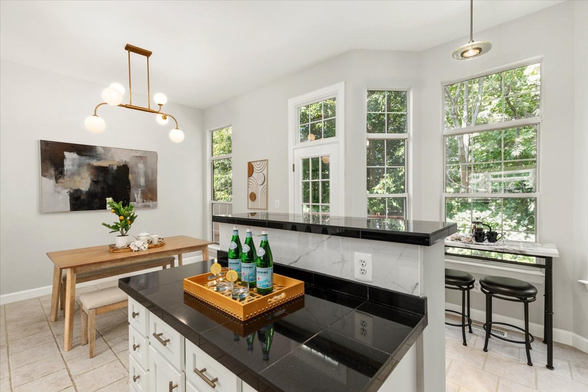 Bright kitchen with a black stone island, raised breakfast bar, and tall windows overlooking greenery.