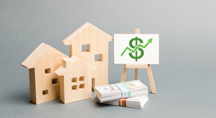Wooden model houses, cash, and a chart with an upward-trending dollar sign.