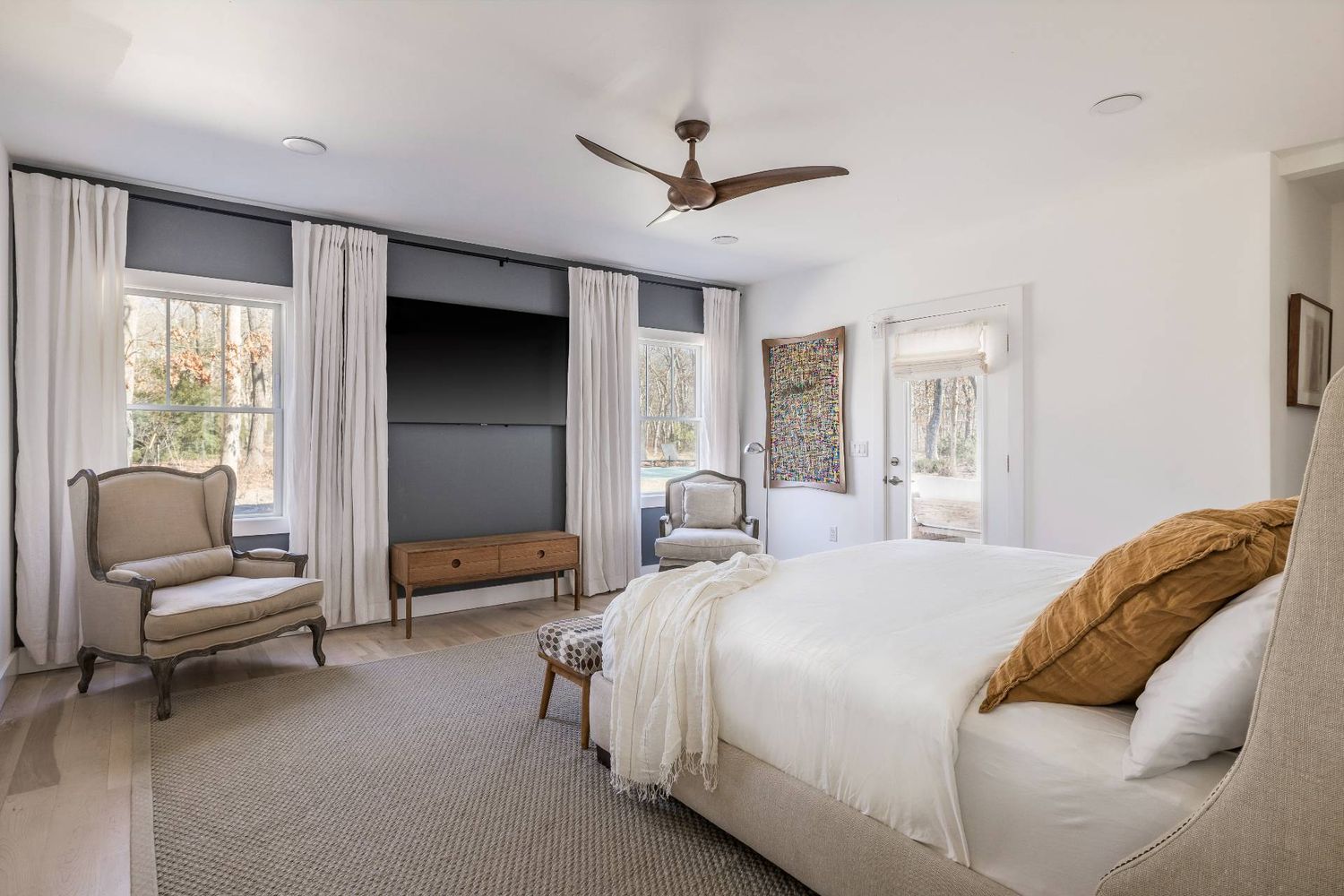 Furnished bedroom with a large bed, curtained windows, built-in TV wall, and ceiling fan.
