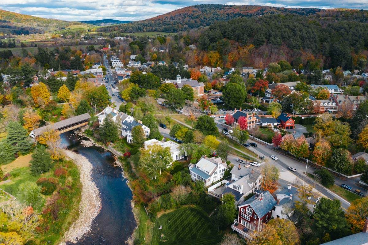 A Vermont village in autumn, with a river winding past buildings and colorful wooded hills.