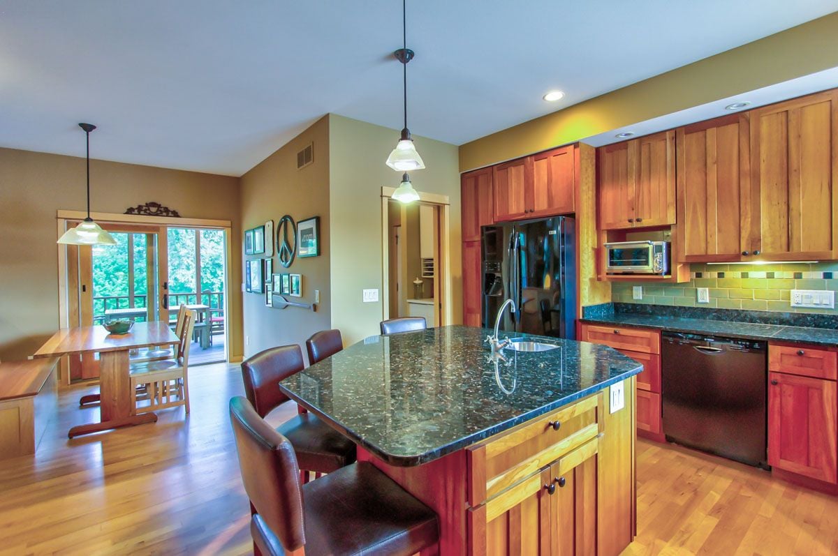 Open-plan kitchen with a granite island, warm wood cabinets, and dining area beside deck doors.