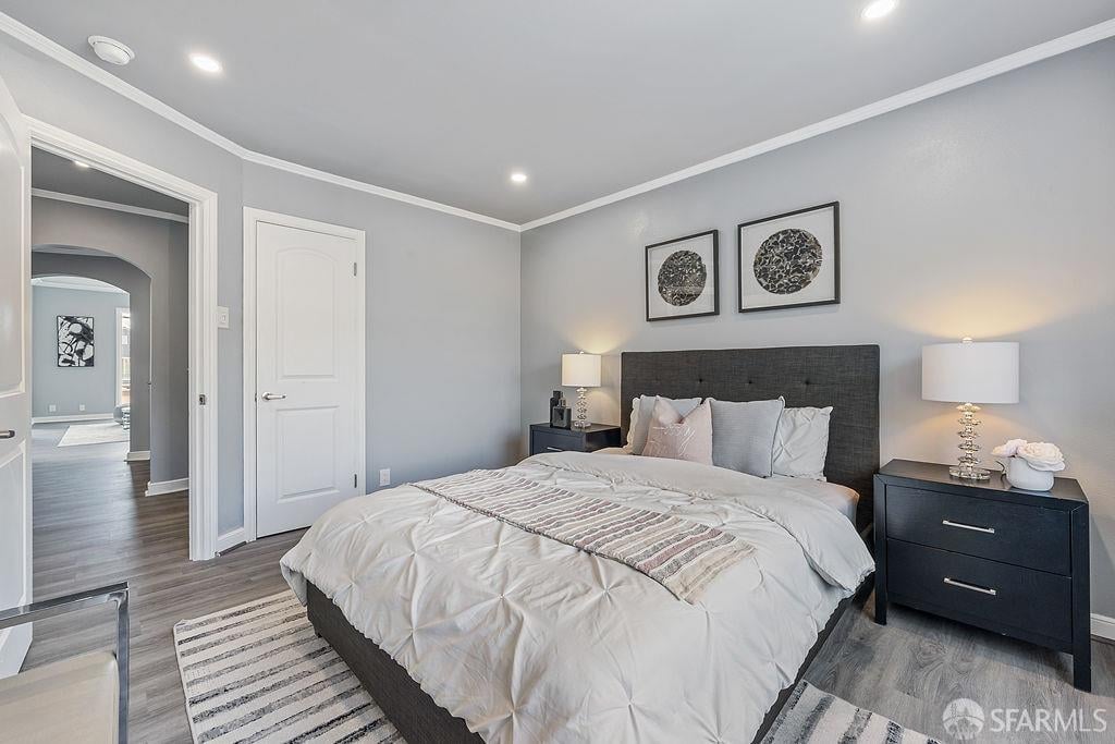 Staged bedroom with a large bed, dark headboard, matching nightstands, and gray wood flooring.