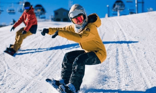A skier in a mustard-yellow jacket carves down a snowy slope as another skier follows.