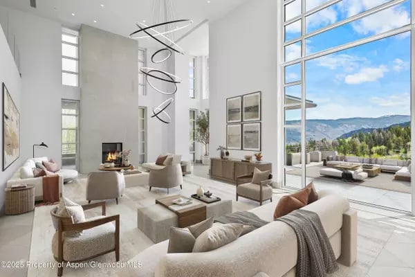 Bright living room with soaring ceilings, a fireplace, and mountain views through expansive windows.