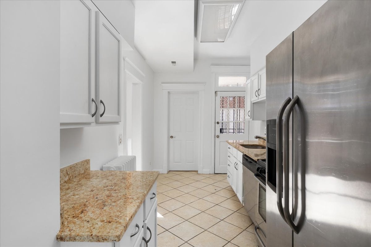 Narrow kitchen with granite counters, white cabinets, stainless-steel appliances, and a security-grille door.