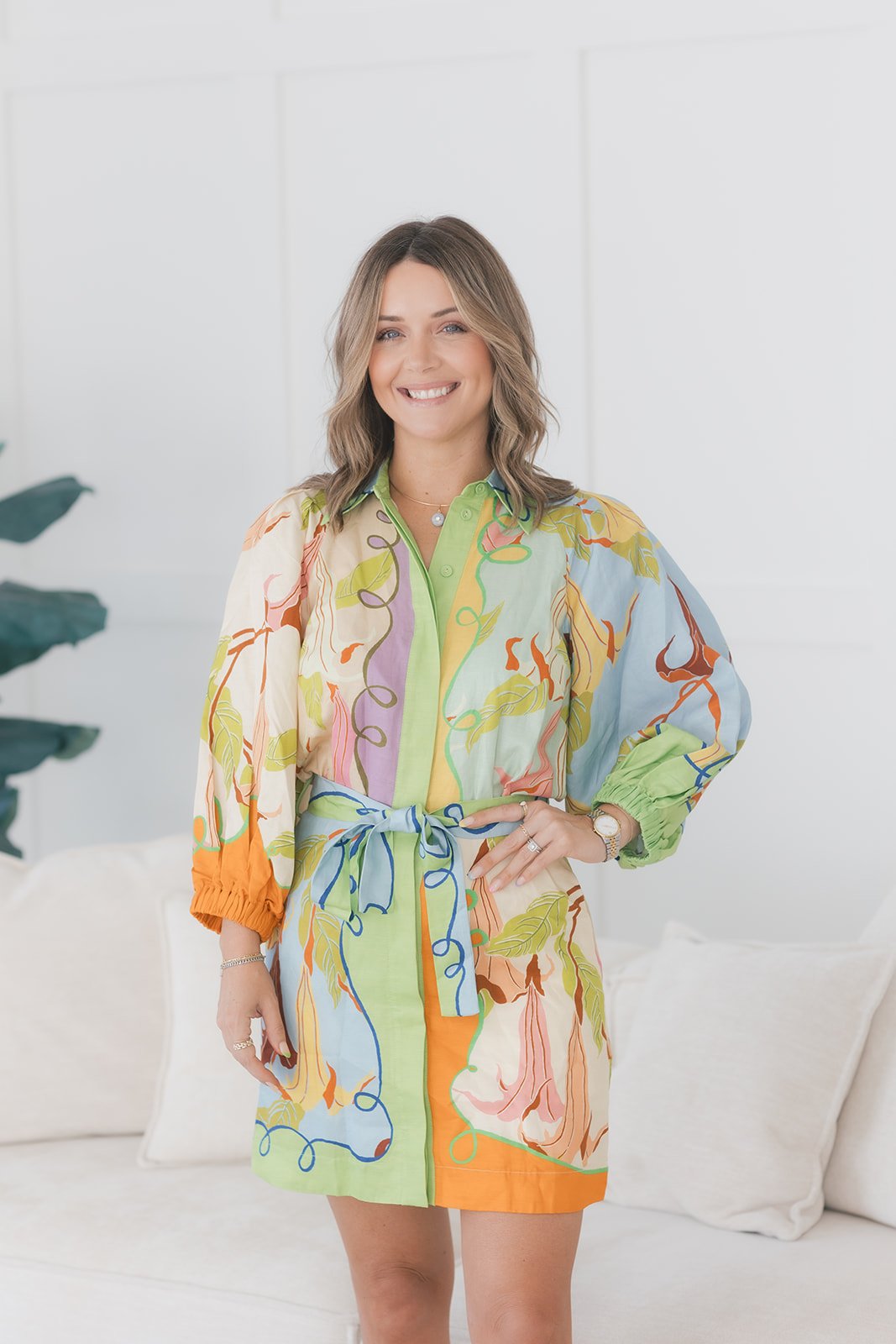 Aubrey Wessolowski smiling in a colorful patterned dress beside a white sofa.