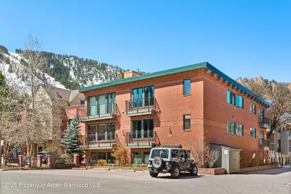 Red-brick building with balconies and a green roof, backed by a snow-dusted mountain.