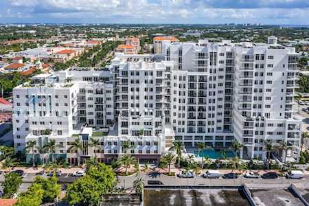 White multi-story condominium with balconies, a pool, palm trees, and a canal in the foreground.
