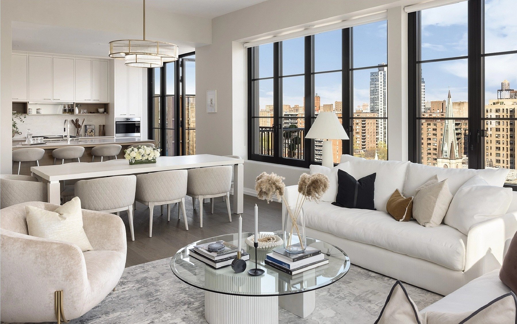 Open-plan living room and kitchen with large city-view windows and white furnishings.
