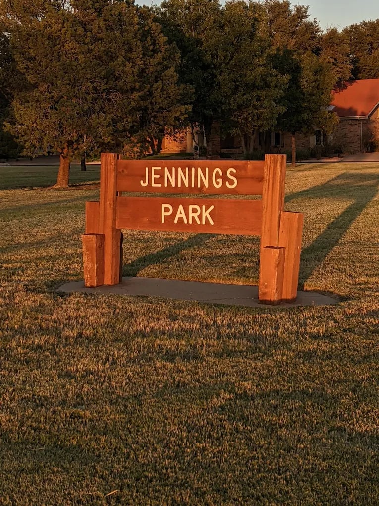 Jennings Park sign on a grassy lawn beneath mature trees.