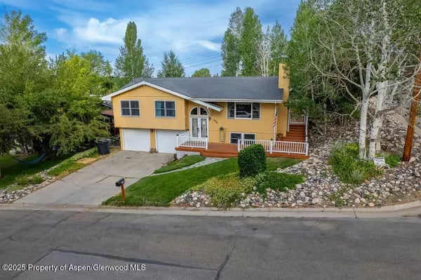 Yellow split-level home with attached garage, white porch railing, and landscaped rock garden.