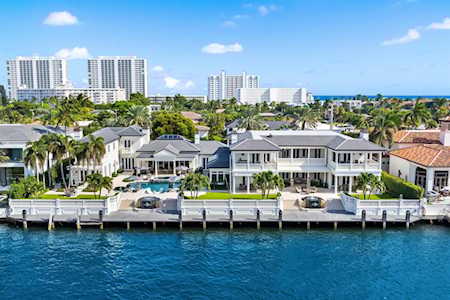 Waterfront homes with private docks along a blue canal, with palm trees and high-rises beyond.