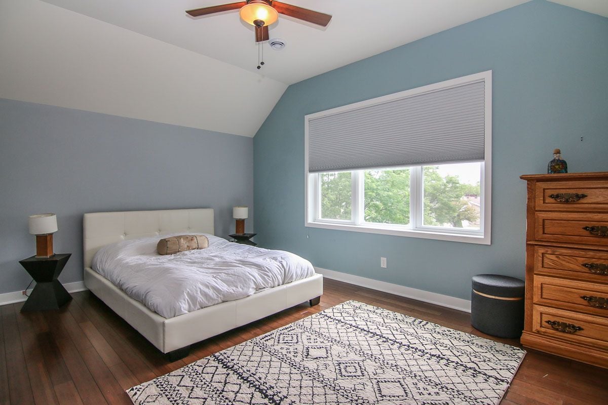 Bedroom with a white upholstered bed, blue-gray walls, and a large window with a raised blind.