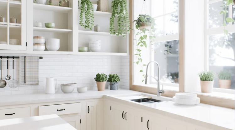 Bright white kitchen with open shelves, subway tile, large windows, and potted plants.
