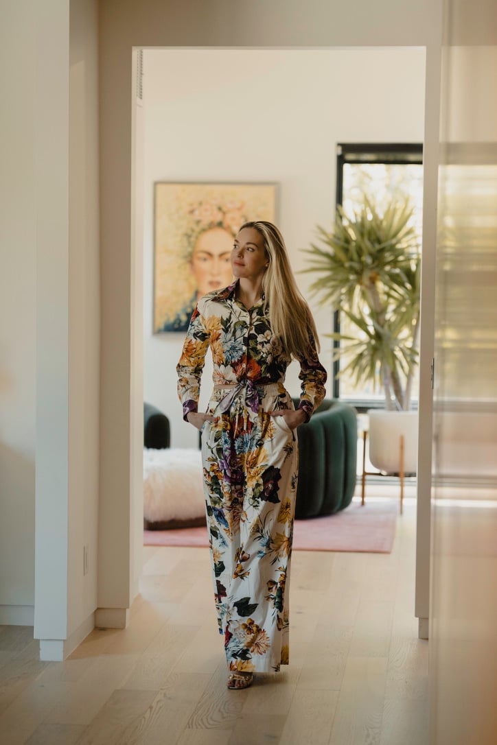 A woman in a colorful floral outfit stands in a bright modern living room.